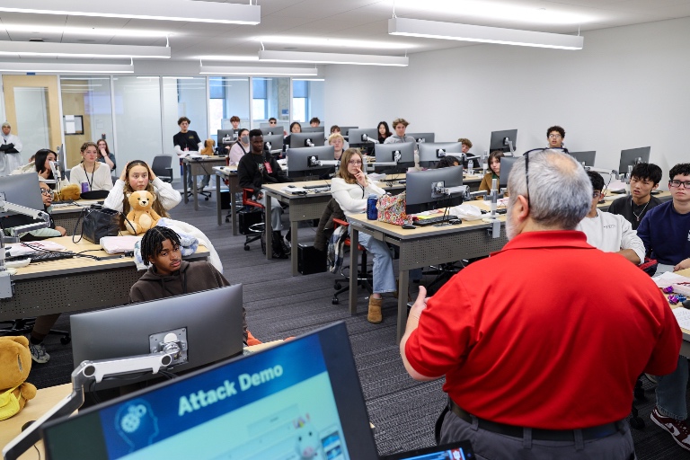 A presenter talks to a group of students, with a slide titled "Attack Demo" in the foreground